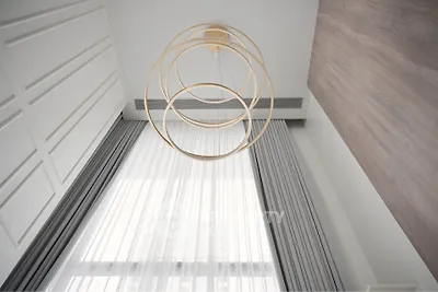 Elegant modern interior with high ceiling and stylish chandelier, featuring floor-to-ceiling curtains.