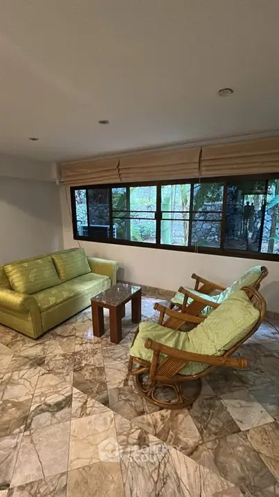 Charming living room with green sofa and rocking chairs, featuring large windows and marble flooring.