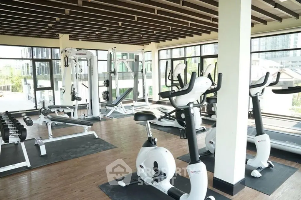 Spacious gym with modern exercise equipment and large windows offering natural light.