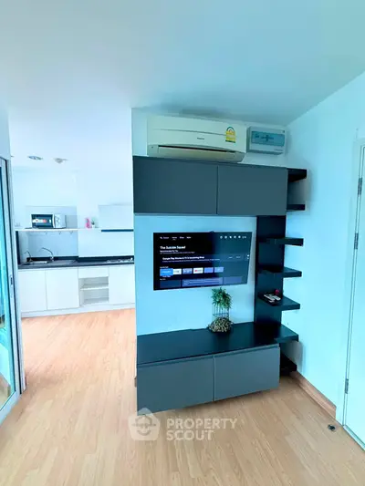 Modern living room with sleek TV unit and air conditioning, open kitchen layout, and stylish wooden flooring.