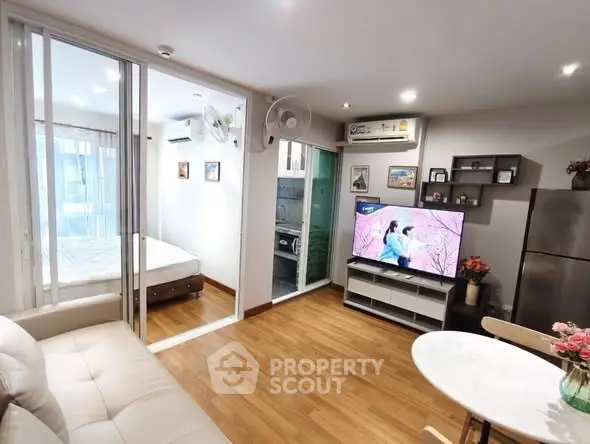 Modern apartment interior with open living room and bedroom, featuring sleek furniture and wooden flooring.