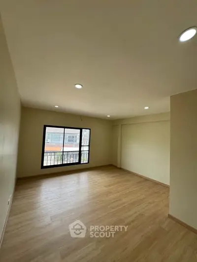 Spacious empty room with wooden flooring and large window, perfect for customization.