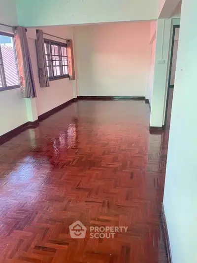 Spacious empty room with polished wooden floors and large windows.