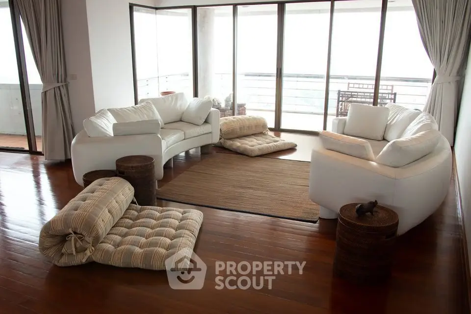 Spacious living room with modern white sofas and large windows overlooking balcony.