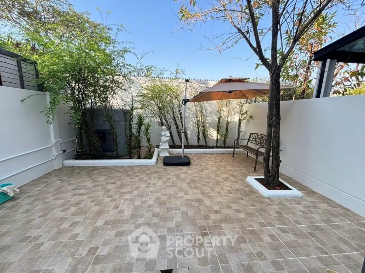 Charming garden patio with tiled flooring, bench, and umbrella, perfect for outdoor relaxation.