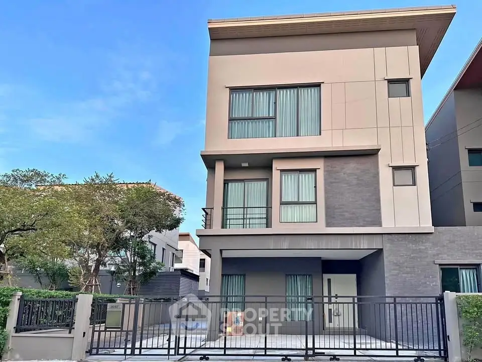 Modern three-story house with sleek design and gated entrance in a serene neighborhood.