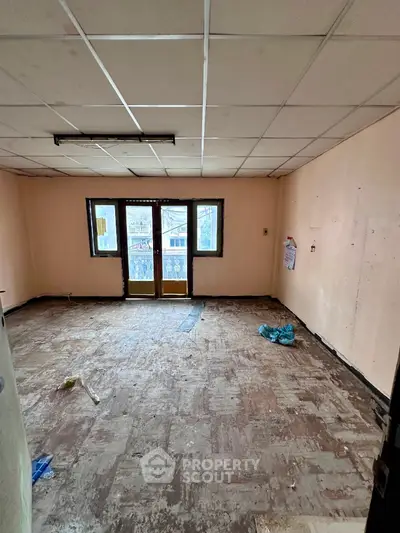Spacious empty room with large windows and tiled ceiling, ideal for renovation.