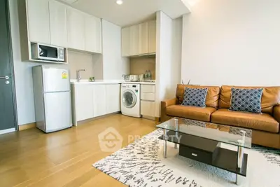 Modern living room with integrated kitchen, featuring a leather sofa, glass coffee table, and appliances.