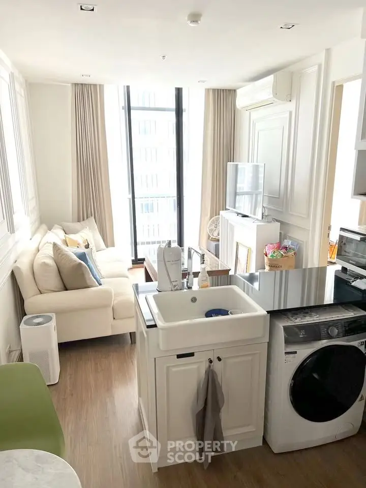 Modern open-layout living room with integrated kitchen and laundry area, featuring sleek design and natural light.