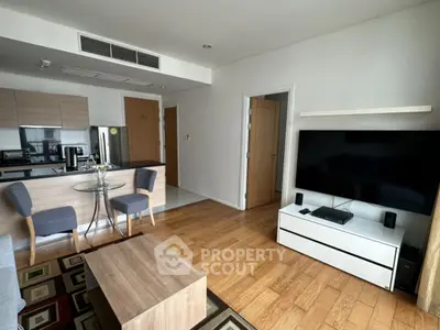 Modern living room with open kitchen, wooden flooring, and large TV setup.