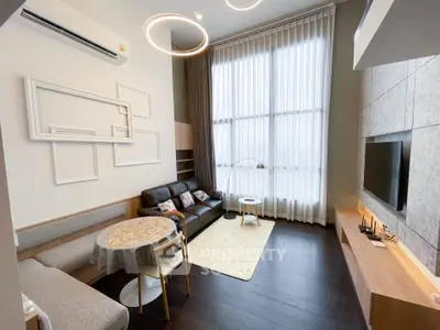 Modern living room with high ceilings, stylish lighting, and large windows for natural light.