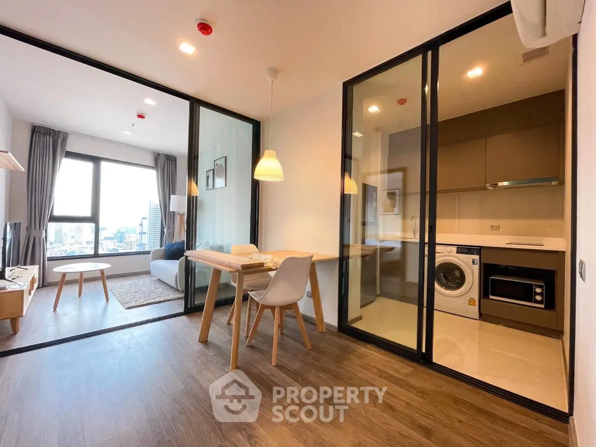 Modern open-plan living room with glass partition, dining area, and kitchen featuring built-in appliances.