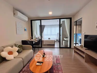 Modern living room with cozy decor and view into a stylish bedroom through glass doors.