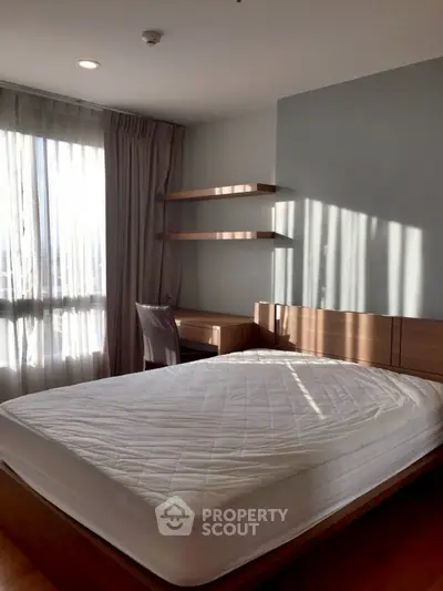 Modern bedroom with natural light, featuring a bed, desk, and shelves.