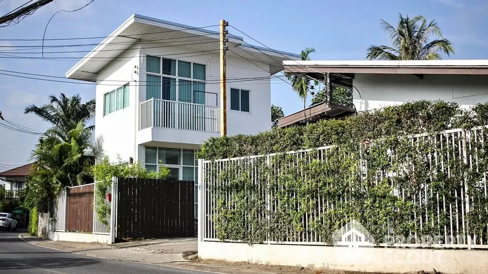 Charming two-story modern home with a lush green hedge fence, featuring a spacious balcony and large windows for ample natural light.