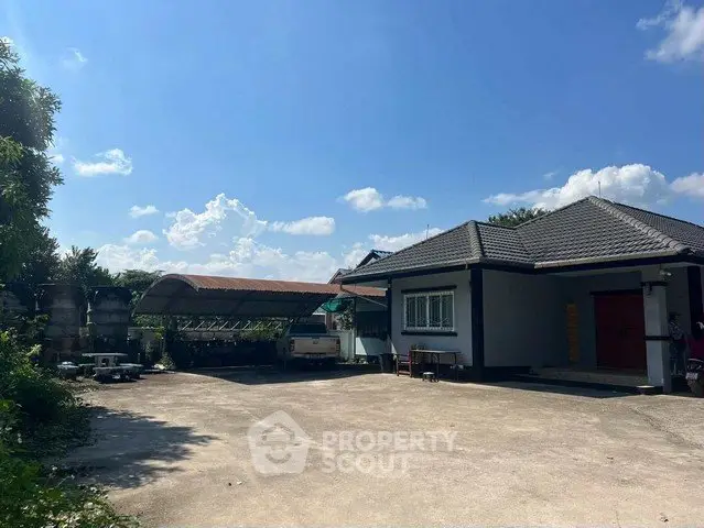 Charming single-story home with spacious driveway and lush greenery under a clear blue sky.
