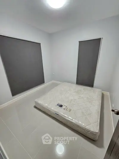 Minimalist bedroom with mattress on tiled floor and large windows with blinds.