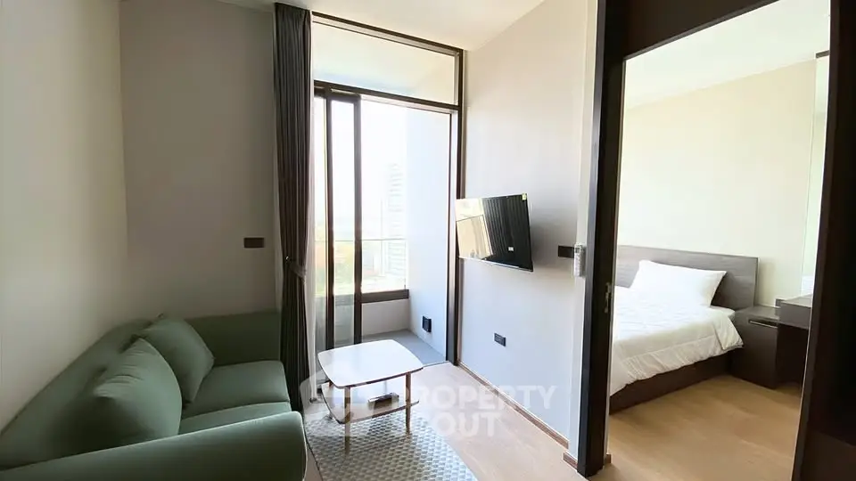 Modern apartment living room with green sofa and wall-mounted TV, adjacent to a cozy bedroom.