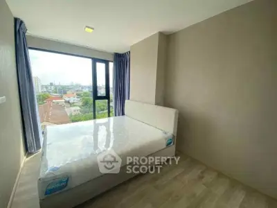 Bright bedroom with large window offering city view, featuring a new mattress and modern decor.