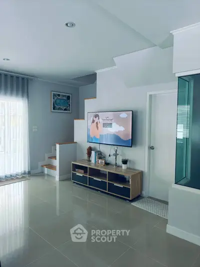 Modern living room with sleek TV unit and staircase, featuring elegant decor and natural light.