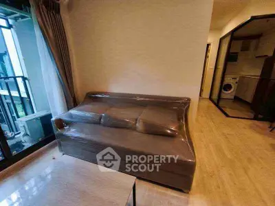 Modern apartment interior with plastic-wrapped sofa and view of compact kitchen area.