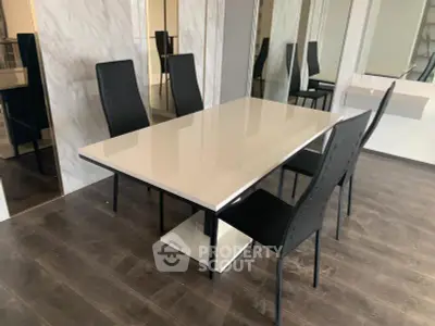 Modern dining area with sleek black chairs and glossy white table on dark wood flooring.