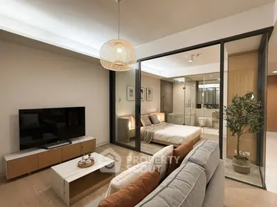 Modern open-concept living room with stylish decor and glass-walled bedroom