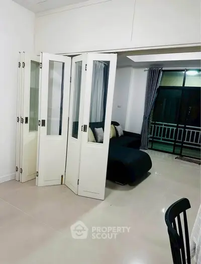 Modern living room with foldable glass doors and sleek black sofa, leading to a balcony with curtains.