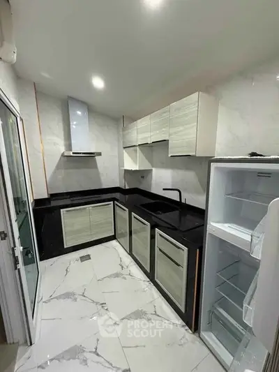 Modern kitchen with sleek black countertops and open fridge in stylish apartment.