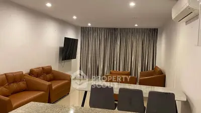Modern living room with leather sofas, wall-mounted TV, and dining area.