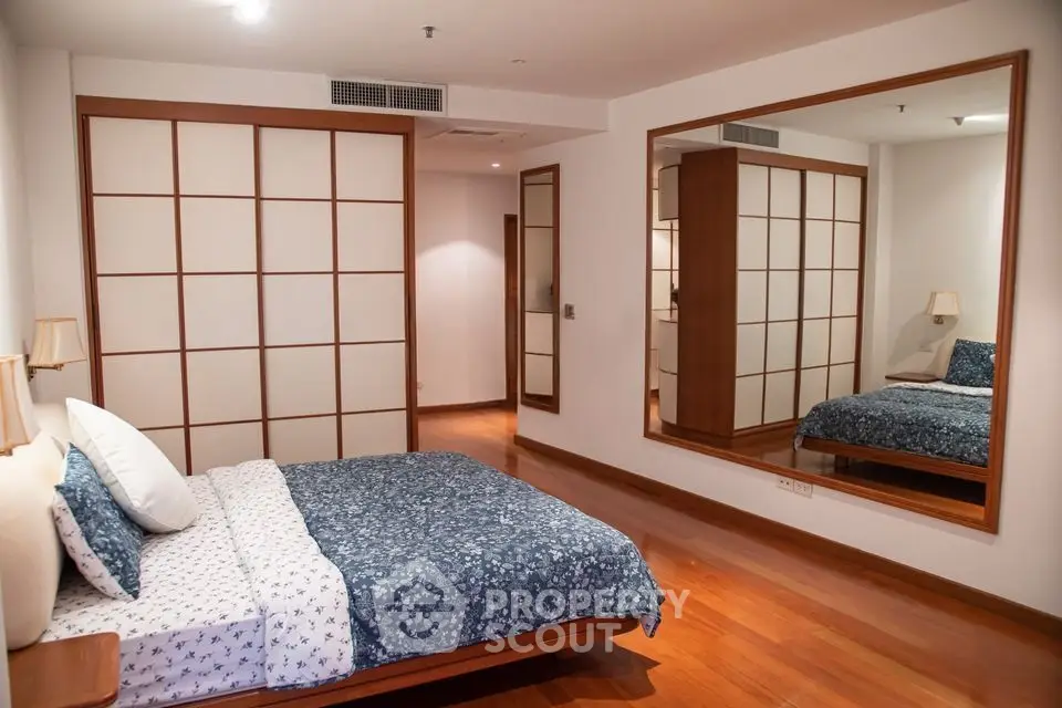 Spacious bedroom with wooden flooring and large mirror