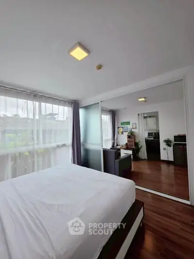 Modern bedroom with large windows and wooden flooring, adjacent to a stylish kitchen area.