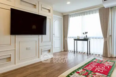 Elegant living room with large TV, stylish paneling, and bright natural light from large windows.