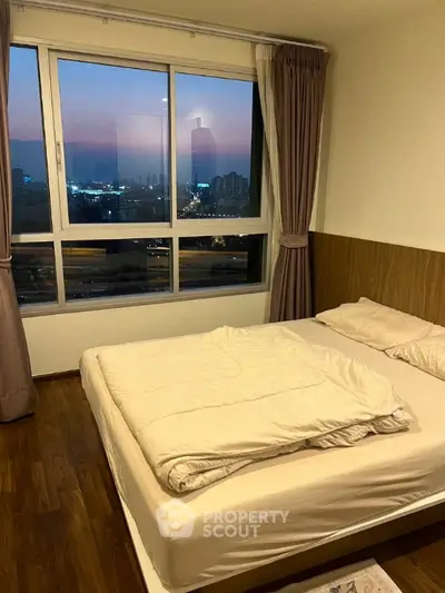 Cozy bedroom with city view, featuring large window and elegant curtains, perfect for urban living.