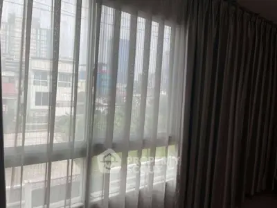 Spacious room with large window and sheer curtains offering a city view.