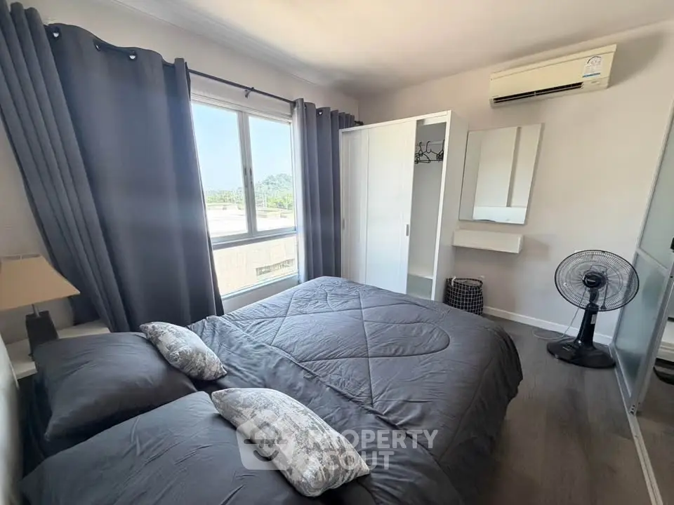 Modern bedroom with large window and air conditioning, featuring stylish gray decor and ample natural light.