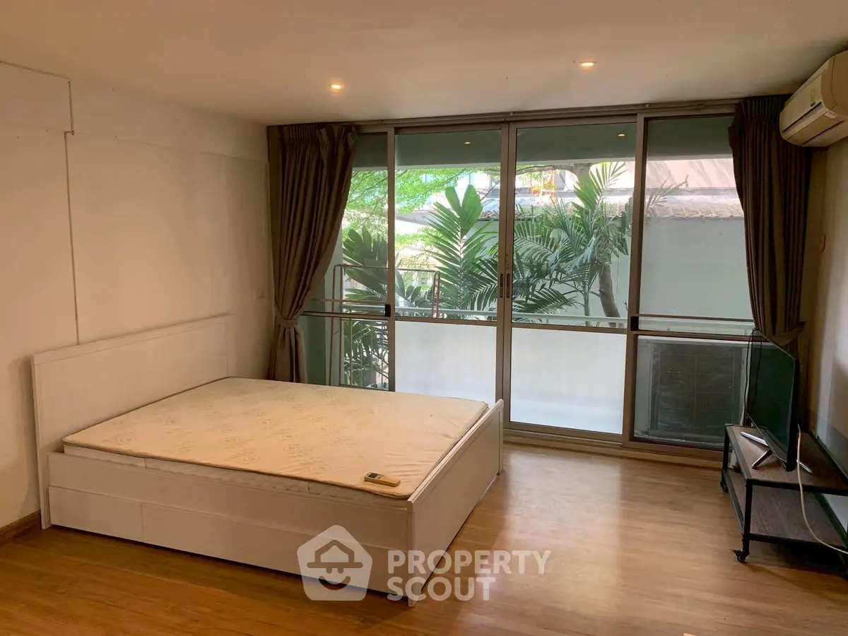 Spacious bedroom with large windows and garden view, featuring a minimalist design and ample natural light.