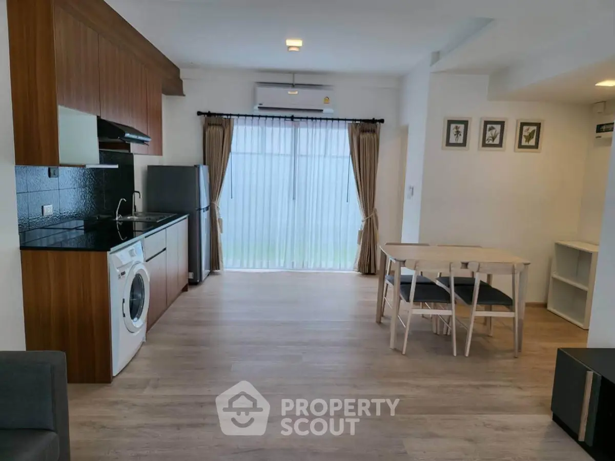Modern open-plan living room with kitchen and dining area, featuring wooden flooring and natural light.