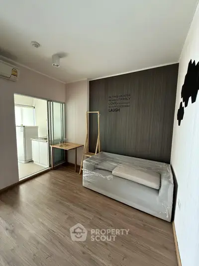 Modern studio apartment with minimalist design and cozy bed, featuring a compact kitchen area.