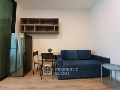 Modern living room with blue sofa, dining table, and stainless steel fridge