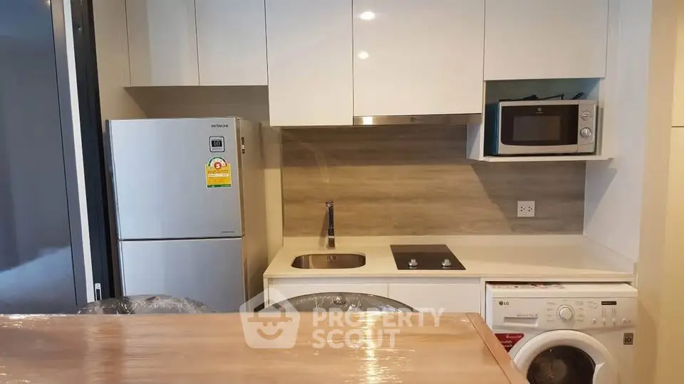 Modern kitchen with sleek appliances including fridge, microwave, and washing machine in compact layout.