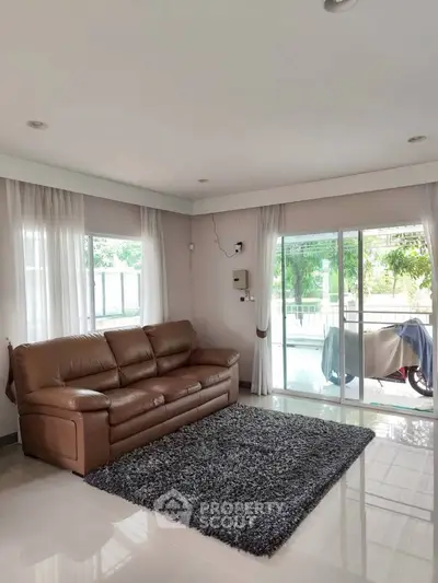 Spacious living room with leather sofa and large windows overlooking greenery.