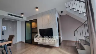 Modern duplex living room with stylish staircase and mounted TV, featuring open kitchen layout.