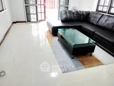 Spacious living room with modern black leather sofa and glass coffee table, perfect for relaxation.