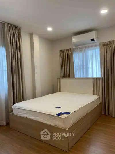 Modern bedroom with wooden flooring, large windows, and air conditioning unit.