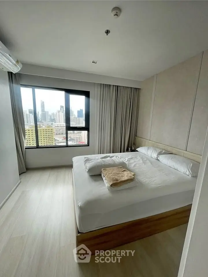 Modern bedroom with city view and natural light in high-rise apartment.