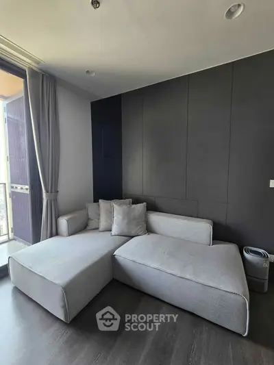 Modern living room with sleek gray sofa and floor-to-ceiling windows offering natural light.