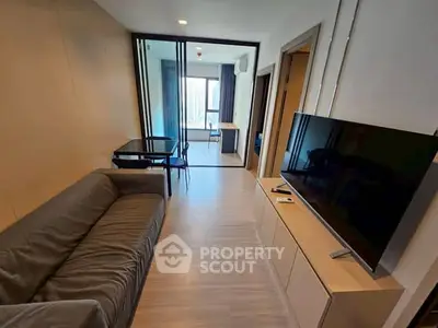 Modern living room with sleek furniture and large TV, featuring a view into a bright bedroom.