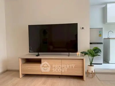 Modern living room with sleek TV stand and open kitchen layout, featuring a stylish fridge and potted plant.