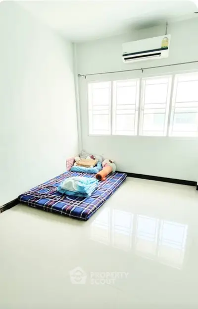 Minimalist bedroom with mattress on floor and large window, bright and airy space.